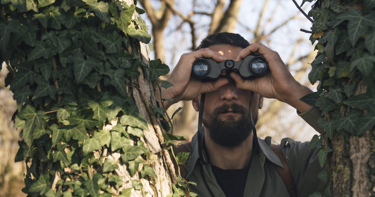 Man in the forest looks through binoculars